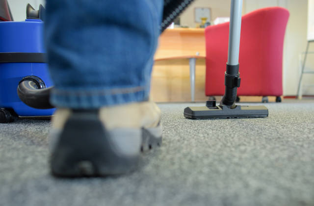 Closeup of vacuum and shoes as a cleaner hoovers the floor